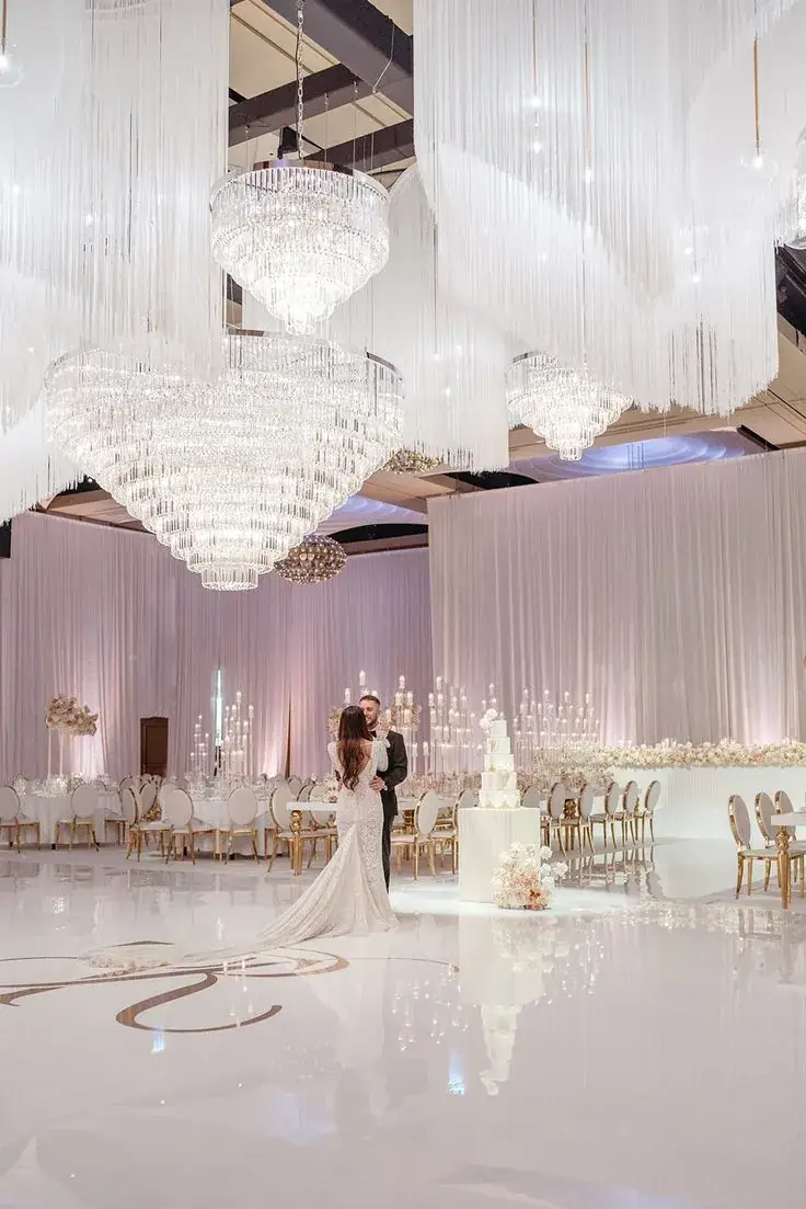 Couple under crystal chandeliers in a white draped hall